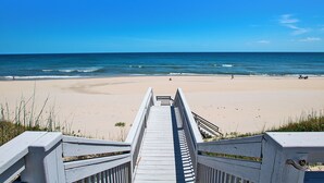 Une promenade en bois mène à une plage de sable, avec l’océan en toile de fond.