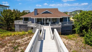 Une maison située en bord de mer, dotée d’un porche couvert, d’une terrasse en bois et offrant une vue sur l’océan.