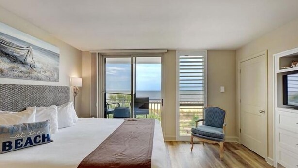 Hotelkamer met een bed, een stoel, een schilderij en een balkon met uitzicht.