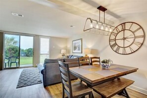 Enjoy meals in this dining area with a large table and chairs, a unique wall clock, and sliding glass door leading to an outdoor space with a view.