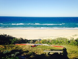 Enjoy a serene beach experience with a clear ocean view, a grassy area, and a wooden bench.