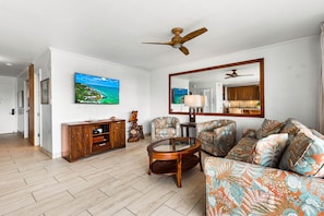 A living room with a large flat-screen TV, a ceiling fan, a sofa, a coffee table, and a wooden cabinet.
