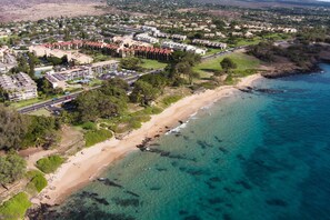 An aerial view of a coastal resort with multiple hotel buildings, a sandy beach, and clear turquoise waters.