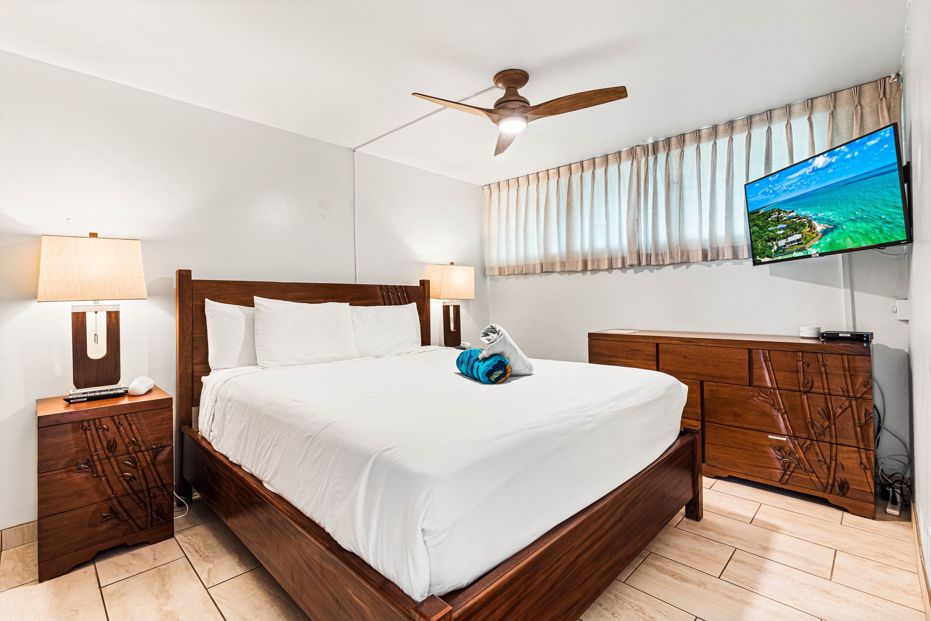 Een hotelkamer met een houten bed, een plafondventilator, een televisie aan de muur en een houten dressoir.