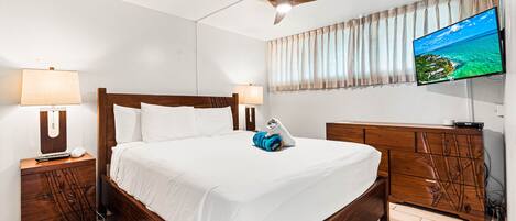 Een hotelkamer met een houten bed, een plafondventilator, een televisie aan de muur en een houten dressoir.