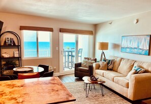 A living room with a large window, a sofa, a coffee table, and a bookshelf. - Come Experience Fall at the Beach! 🍁🏖️☀️🌊 (Pensacola)