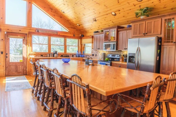 A spacious kitchen with a large island, wooden cabinets, and a refrigerator. - Log Lover's Dream on Sand Point (Pigeon)