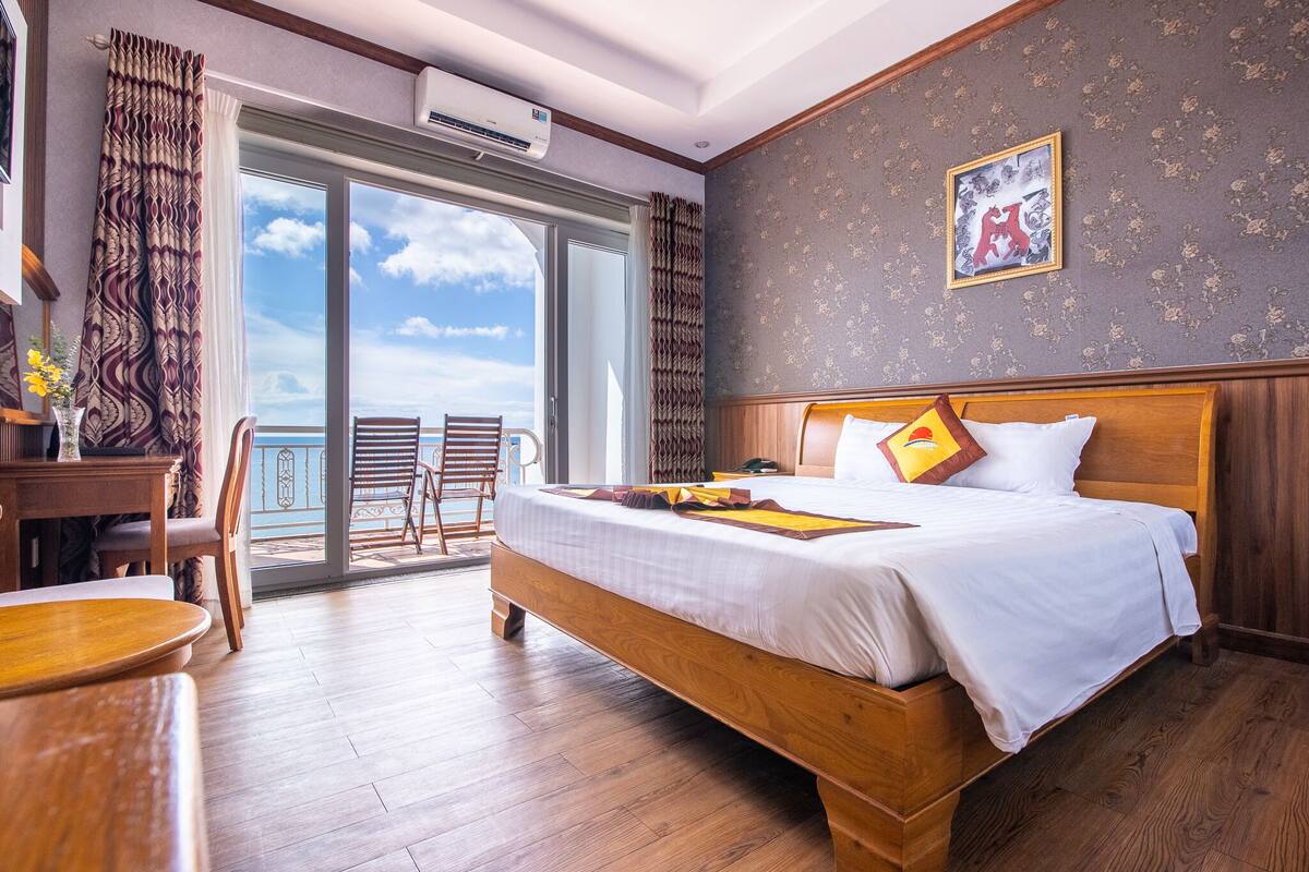 Hotellihuone, jossa on suuri sänky, puinen työpöytä, tuoli ja parveke, jolta on näkymä.