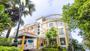 Een meerlaags hotel met een overdekte ingang, een kleurenschema van wit en geel, en een aangelegde tuin met palmbomen.
