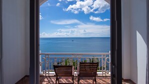 Een balkon met twee houten stoelen, gericht op uitzicht over de zee door een rondboogvormige deuropening.