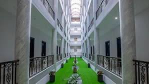 Een hotelgang met marmeren zuilen, kunstgras, potplanten en een centrale doorgang.
