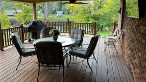 A covered outdoor patio with a round table and chairs, a grill, and a view of a backyard.