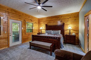 Et soveværelse med træpaneler, seng, to sengeborde med lamper, bænk og loftsvagt.