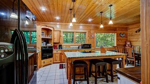 A spacious kitchen with wooden cabinets, a granite countertop, and a central island with stools. - Arrowhead Lodge #568 (Gatlinburg)