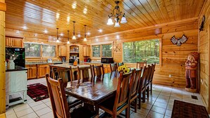 A wooden cabin interior with a dining area, kitchen, and large windows. - Arrowhead Lodge #568 (Gatlinburg)