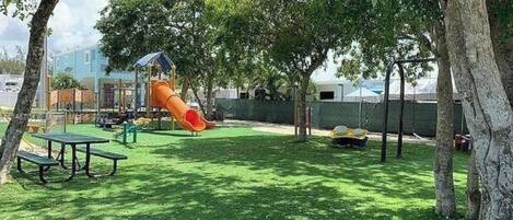 A playground with a slide and picnic tables in a grassy area.