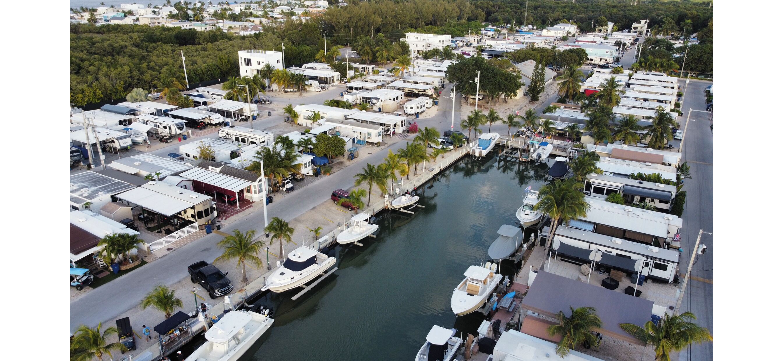 A marina with RVs and boats docked along a waterway, surrounded by buildings and palm trees.