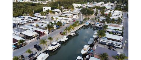 A marina with RVs and boats docked along a waterway, surrounded by buildings and palm trees.