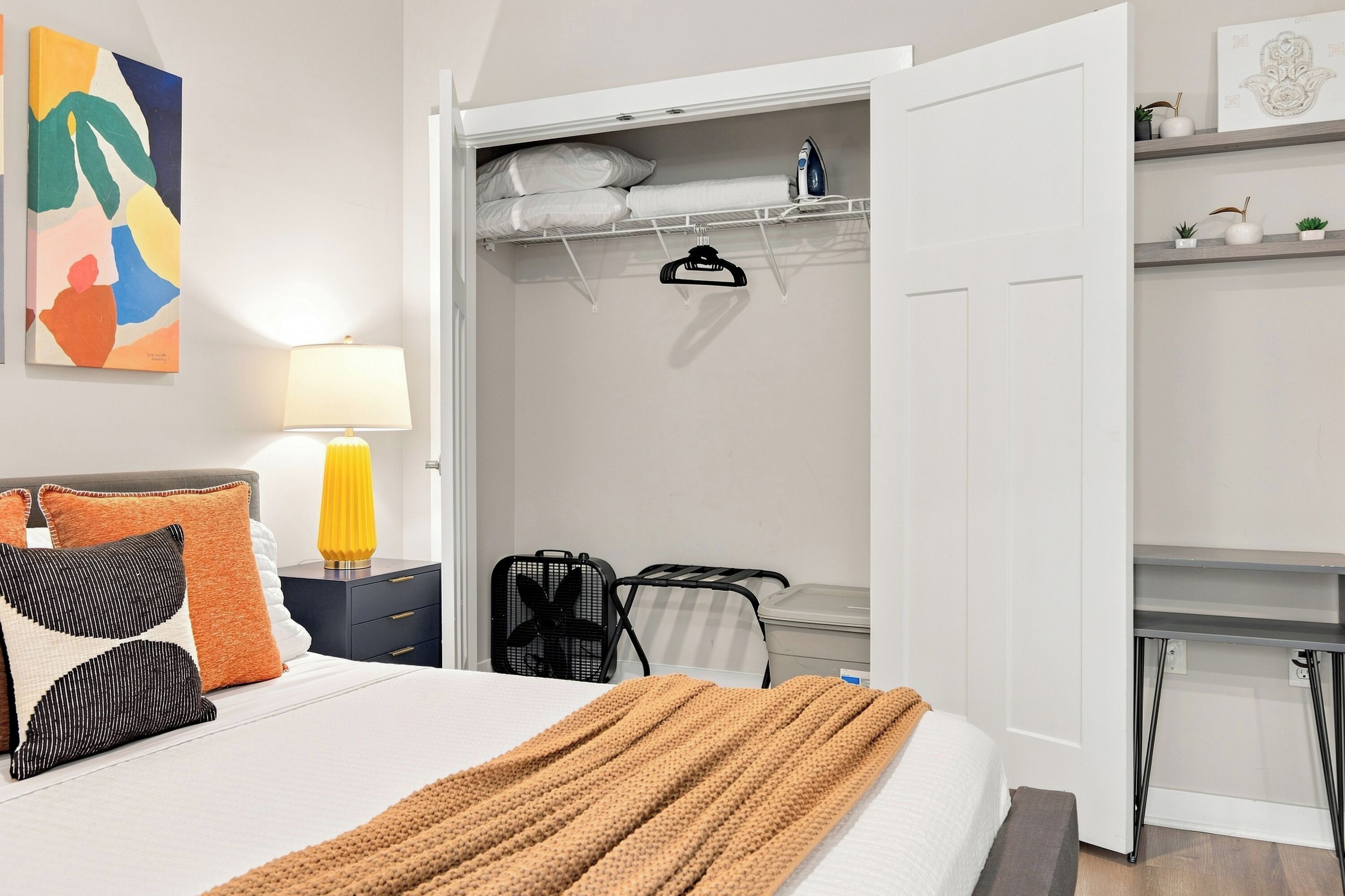 Habitación de hotel con cama, mesita de noche, lámpara y armario con espacio para colgar ropa.
