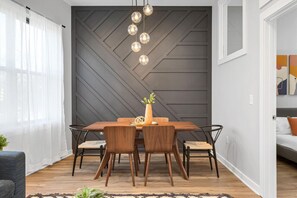 A modern dining area with a wooden table and chairs, a geometric wall design, and pendant lighting.