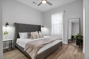 A modern bedroom with a large bed, bedside lamps, a ceiling fan, and a large mirror.