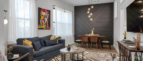 Una sala de estar moderna con un sofá gris, una mesa de centro redonda y un comedor con una mesa y sillas de madera.