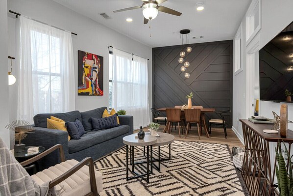 A modern living room with a grey sofa, a round coffee table, and a dining area with a wooden table and chairs.