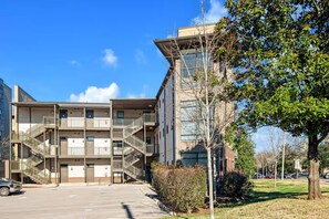A multi-story residential building with external staircases, a parking lot, and a tree-lined street.