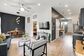 A modern living space with a dining area, a seating area with a coffee table, a television, and a kitchen with a refrigerator.