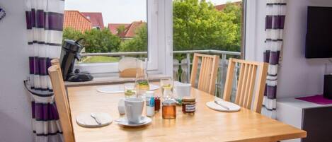 A dining area with a wooden table, chairs, and a view of greenery and buildings outside.