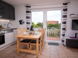 A modern kitchen with a dining area, a balcony with a view, and a TV on the wall.