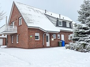 A two-story brick building with a snow-covered roof, a balcony, and a small window.