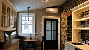 Una cocina con pared de piedra, una puerta negra, una mesa de comedor con sillas y un ventanal con lámpara colgante.