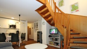 Una sala de estar con una escalera de madera, un comedor, una cocina y un televisor sobre una repisa.