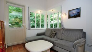 Una habitación con un sofá gris, una mesa blanca, un ventanal con cortinas y un cuadro colgado en la pared.