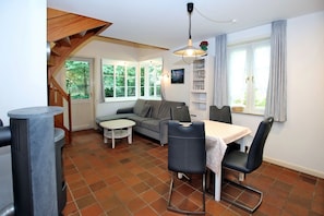A cozy living area with a sofa, a dining table with chairs, a fireplace, and a staircase. - Gmelinstraße 19 d - Hausscheibe mit 2- Zimmern auf ca. 52m² und Terrasse (Wyk auf Föhr)