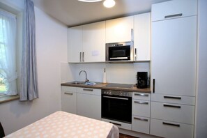 A compact kitchen with a microwave, stove, and coffee maker. - Gmelinstraße 19 d - Hausscheibe mit 2- Zimmern auf ca. 52m² und Terrasse (Wyk auf Föhr)