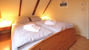 A double bed with white linens and towels, wooden headboard, bedside table with lamp, and a framed picture on the wall. - Ginsterweg 1b, Whg. 2 - Holiday apartment with 2 rooms (Wyk auf Föhr)