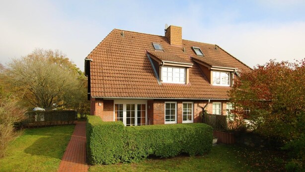 Een herenhuis met twee verdiepingen, een bakstenen gevel, een pannendak en een verzorgd gazon.