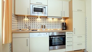 Een compacte keuken met witte kastjes, een magnetron, een koffiezetapparaat, een vaatwasser en een oven.