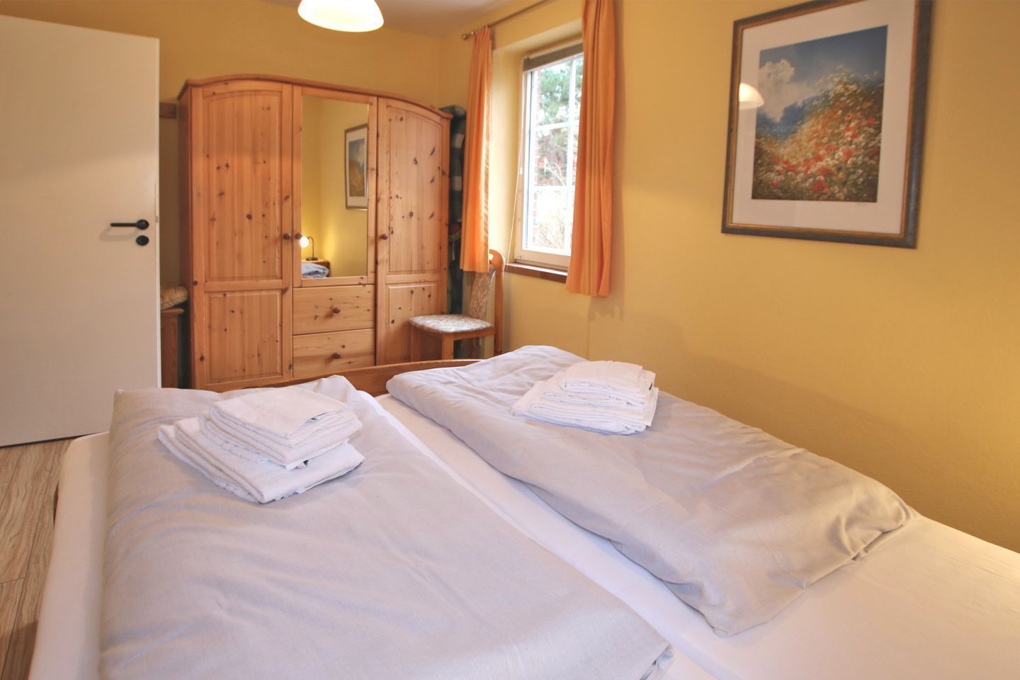 Habitación de hotel con dos camas, un armario de madera, una ventana con cortinas y un cuadro enmarcado en la pared.