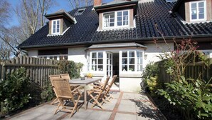 A house with a tiled roof, a fenced garden, and a patio with a table and chairs.