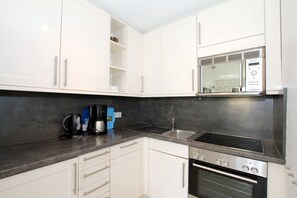 A modern kitchen with white cabinets, a stainless steel sink, a built-in oven, and a coffee maker.