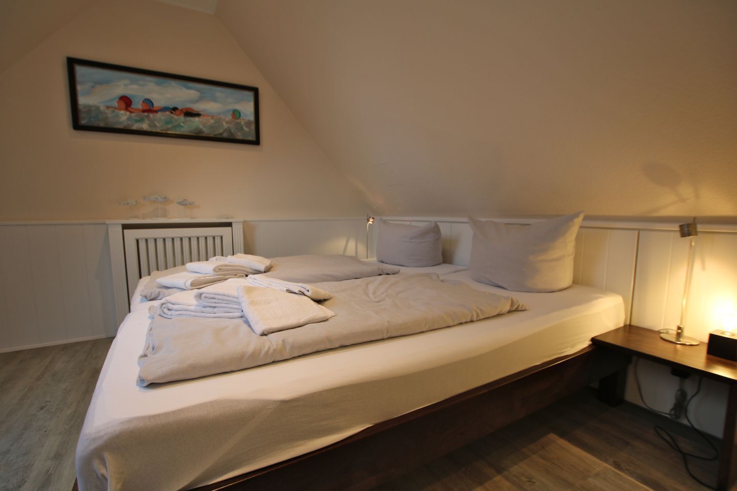 Un lit simple avec du linge de lit blanc, une table de chevet avec une lampe et un tableau au mur.