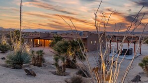 Paisaje desértico con una casa que tiene un patio, rodeado de cactus y plantas del desierto.
