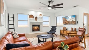 Amplia sala de estar con chimenea, sofá de cuero y comedor con televisor.