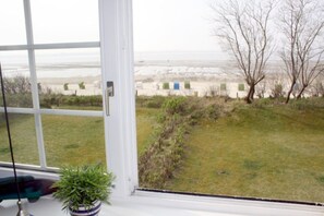 Blick aus einem Fenster auf eine Wiese mit Strand und einem Zaun in der Ferne.
