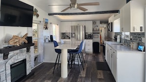 A modern kitchen with white cabinets, a built-in oven, and a dining area with a stone fireplace. - Waterfront Canal Cottage, Kayaks & Canoes, Minutes from Springs & Manatees! (Crystal River)