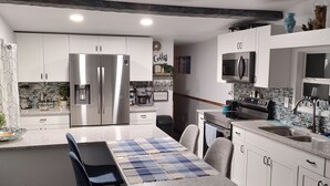 A modern kitchen with white cabinets, stainless steel appliances, and a central island with a blue and white checkered tablecloth. - Waterfront Canal Cottage, Kayaks & Canoes, Minutes from Springs & Manatees! (Crystal River)