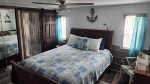 A bedroom with a bed, a ceiling fan, a wooden headboard, a wall anchor decoration, and a window with curtains. - Waterfront Canal Cottage, Kayaks & Canoes, Minutes from Springs & Manatees! (Crystal River)